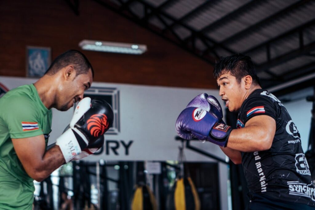 To mænd træner i en livlig Muay Thai session, der viser færdigheder og intensitet indendørs.






